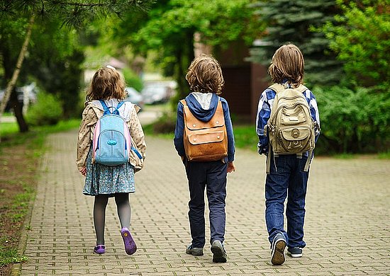 Foto von drei Kindern, die Schulrucksäcke tragen. 